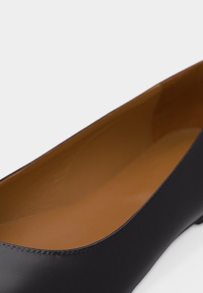 Μαύρο δερμάτινο επίπεδο παπούτσι με καφέ εσωτερική επένδυση, στρογγυλερή μύτη και χαμηλό τακούνι, εμφανιζόμενο σε κοντινή λήψη σε λευκό φόντο.