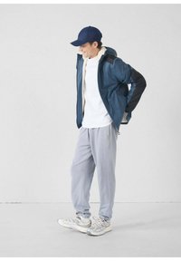 Chaqueta azul marino con capucha y detalles en negro, camiseta blanca, pantalones deportivos gris claro y zapatillas reflectantes. Tela suave, ajuste informal.