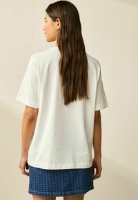 Weißes Baumwoll-T-Shirt mit lockerer Passform, kurzen Ärmeln und Rundhalsausschnitt, kombiniert mit einem blauen karierten Jeansrock.
