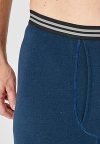 Bóxer azul marino hecho de una tela suave y elástica, con una cinturilla elástica negra que presenta dos franjas grises. Costuras planas visibles.