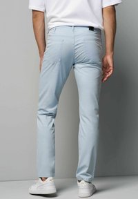 Lichtblauwe, slim-fit broek van rekbaar materiaal. Voorzien van achterzakken en een gladde textuur, gecombineerd met witte sneakers.