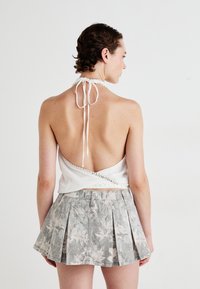 Top bianco con scollo all'americana e dettaglio attorcigliato, abbinato a una gonna a ruota grigia chiara con un sottile motivo a foglie.