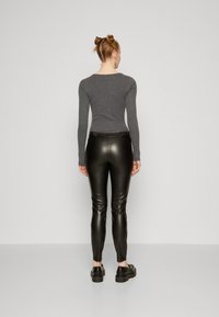 Black faux leather leggings with a fitted design and elastic waistband, paired with a fitted grey long-sleeve top, viewed from the back.