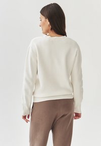 Felpa bianca con scollo rotondo, maniche lunghe e orlo a costine, abbinata a pantaloni marrone chiaro, tessuto morbido, vestibilità rilassata.