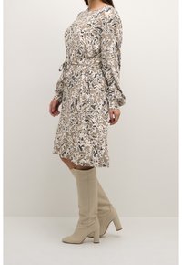 Robe à manches longues à motif floral dans des tons beige et gris, avec une ceinture nouée à la taille. Associée à des bottes à talons hautes jusqu'aux genoux de couleur beige.