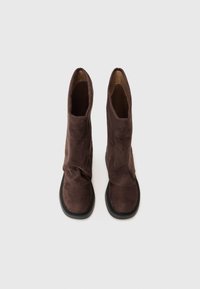 Braune Wildleder-Stiefeletten mit einer schlaffen Form, flachen schwarzen Gummisohlen und abgerundeten Zehen, die eine glatte Textur und minimalen Nähten aufweisen.