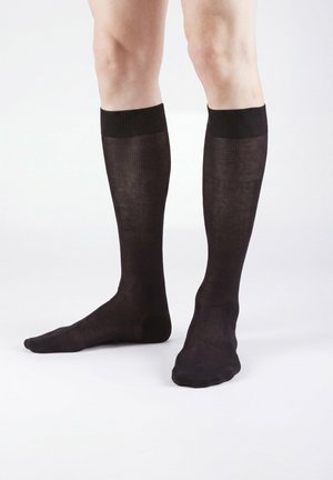 Benen met kniehoogte zwarte doorschijnende sokken met geribbelde bovenkant, staand op een effen witte achtergrond.