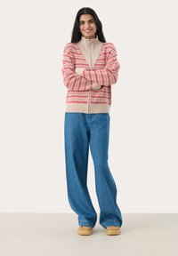 Stickad cardigan i krämfärg med röd geometrisk mönster, hel längd ärmar, ribbade manschetter, tillsammans med ljusblå vida jeans och beige skor.