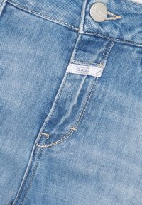Jean en denim bleu clair montrant la poche avant, la passants de ceinture et le bouton métallique avec la marque "CLOSED".