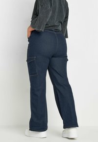 Tummansiniset cargo-housut, joissa on leveät lahkeet, sivutaskut ja kontrastivärinen ompelu. Valmistettu denimmateriaalista, jossa on rento istuvuus.