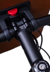 Frenos de bicicleta de metal negro con un soporte Klickfix, con un botón de liberación rojo, marcas de par de torsión claras y cables visibles sobre un fondo marrón.