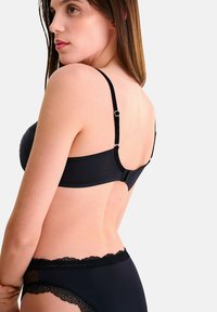 Soutien-gorge noir avec bretelles réglables et fermeture à crochet. Il est doté d'un tissu doux avec une texture à pois et d'une garniture en dentelle le long des bords.