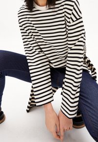 Schwarz-weiß gestreiftes Langarmshirt mit Rundhalsausschnitt, kombiniert mit dunkelblauen Jeans. Das Shirt hat eine lockere Passform und seitliche Bindebänder.