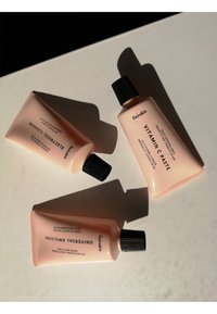 Drei rosa Hautpflege-Tuben auf einer weißen Oberfläche, mit schwarzen Schraubverschlüssen. Auf den Etiketten stehen "Vitamin C Paste", "Electro Forest Cleanser" und "Universal Emulsion".