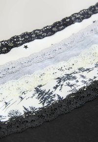 Fem stofstrimler med kant af blonde: sort, lysegrå, hvid med sort skovmønster, creme og mørkegrå. Teksturerede kanter og varierende bredder.