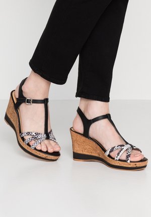 Sandały na koturnie z czarnymi skórzanymi paskami i korkową podeszwą. Część na palce ma krzyżowy wzór w motyw węża.