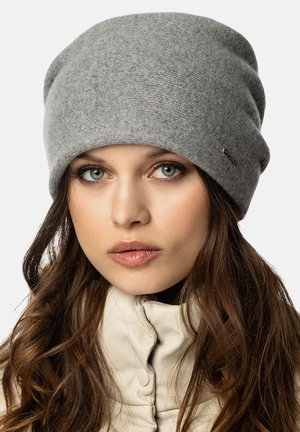 Bonnet en tricot gris avec une texture douce, au design décontracté, et un petit détail en métal. Porté au-dessus du col d'une veste claire.