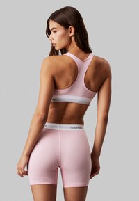 Ružičasti sportski grudnjak i odgovarajuće šortse s bijelom trakom s Calvin Klein logotipom, s racerback dizajnom i glatkom, mekanom teksturom.