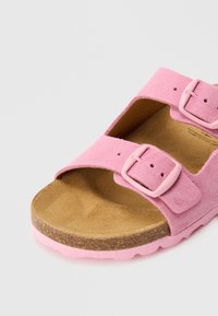 Ružová semišová šľapka so dvoma nastaviteľnými prackami a tvarovanou hnedou korkovou stielkou na svetlom pozadí.