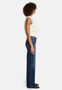 Top bianco senza maniche con una texture morbida, abbinato a jeans in denim blu scuro a vita alta, fit dritto, e scarpe nere.