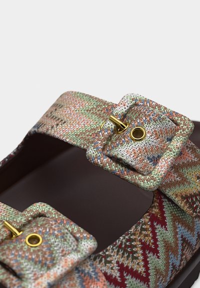 Sandale à bout ouvert avec des brides en tissu tricoté multicolore, dotées de grandes boucles assorties et de fermoirs à goupille en métal doré.