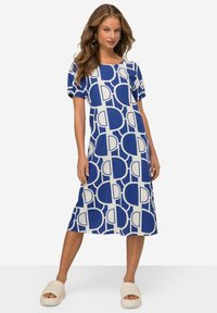 Modrá a bílá šaty se vzorem, s krátkým rukávem, uvolněným střihem a kulatým výstřihem. Nosené s krémovými klouzavými sandály.