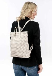 Sac à dos en tissu texturé avec un motif géométrique beige, doté de deux bretelles et d'une poignée supérieure. Détails en métal argenté inclus.