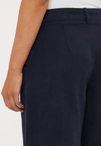 Tumedadest sinine värvi püksid, mis on valmistatud twill-kangast, omades sileda tekstuuri, hästi istuvat lõiget ning külgmisi taskuid, millel on tagasihoidlikud õmblemise detailid.