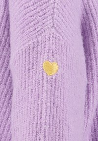 Weicher fliederfarbener Strickstoff mit einem kleinen goldgelben, zentrierten Herz, das auf einem strukturierten Chevron-Muster gestickt ist.