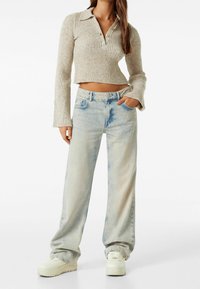 Beige ribbad långärmad kort tröja med krage och knappar. Ljus tvättade vida jeans med en urblekt yta och sidofickor.