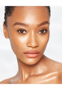 Close-up of a face with smooth, glowing skin. Features include well-defined brows, full lips, and a light sheen. Dark, curly hair is partially visible.