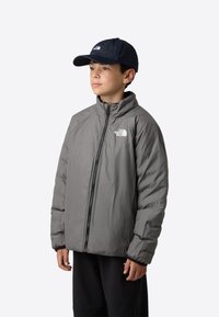 Šedá zateplená bunda s vysokým límcem a celým zipem. Má černé manžety a bílé logo na levé hrudi. Nositelná s tmavou baseballovou čepicí.