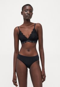 Bralette nera in pizzo con spalline regolabili e bordi ondulati, abbinata a mutandine nere a vita alta con cintura ondulata.
