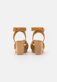 Bruine suède plateau sandalen met een stevige houten hak, voorzien van verstelbare enkelbandjes en ronde uitsparingen aan de zijkanten.