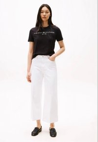 Black cotton t-shirt with a white logo, paired with white wide-leg jeans and black loafers. Simple, casual outfit with clear color contrast.