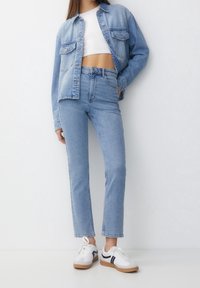 Light blue denim jacket over a white crop top, paired with high-waisted light blue jeans and white sneakers with black stripes.