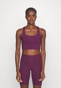 Violeta sporta krūšturis ar īsām piedurknēm un atbilstošas augsto vidukli šortus, kas izgatavoti no elastīga materiāla ar gludu tekstūru un minimālistisku dizainu.