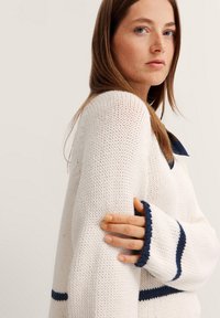 Strickpullover in Creme mit Marineblauen Streifen. Hat eine lockere Passform, gerippte Bündchen und eine weiche Textur. Stylischer Kragen kontrastiert mit der Hauptfarbe.