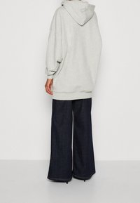 Sudadera de gran tamaño en gris claro con capucha, puños y dobladillo de canalé, combinada con jeans de pierna ancha en azul oscuro que presentan un corte holgado y dobladillos sin terminar.