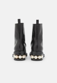 Botas de tobillo de cuero negro con un diseño elegante, que presentan una punta redondeada y un distintivo adorno de perlas blancas en el tacón.
