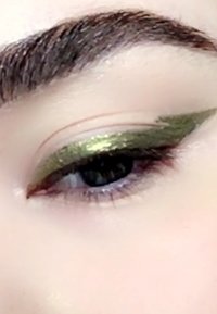 Close-up of an eye featuring green metallic eyeshadow with a sharp wing. The eyelid is softly highlighted with a neutral tone.