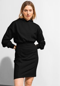 Svart hoodie med avkopplad passform och ribbade manchetter, kombinerad med en figurnära svart penkjol. Materialet verkar mjukt och stretchningsbart.