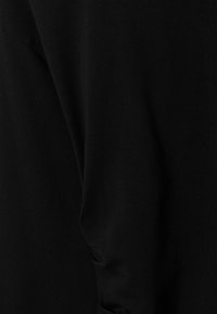 Tissu noir texturé avec une finition lisse, présentant des plis drapés et des coutures, offrant une apparence douce et légère.