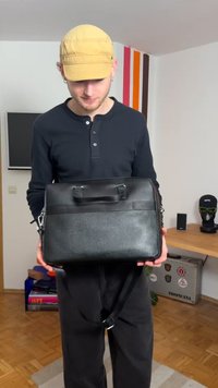 Sort læder messenger taske med to top-håndtag, justerbar rem, glat tekstur og et minimalistisk design.