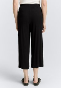 Culottes noires légères avec une taille élastique, présentant une coupe ample qui arrive au milieu du mollet. Portées avec des chaussures noires à enfiler.