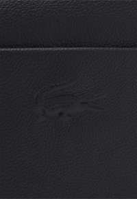 Borsa in pelle nera con una finitura texturizzata, caratterizzata da un logo impresso. Il design è strutturato con dettagli minimi.