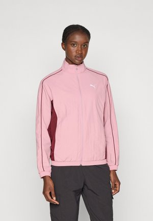 Giacca a track Puma in rosa chiaro con pannelli laterali bordeaux, colletto alto, chiusura con zip e polsini elasticizzati. Caratterizzata da logo sul petto.
