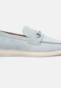 Scarpa slip-on scamosciata azzurra chiara con tomaia texturizzata, dotata di un accento metallico argento e di una suola in gomma beige. Design semplice e piatto.