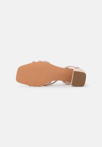 Nude heeled sandal with a textured synthetic sole, slim straps, and a block heel. The sole features horizontal grooves for traction.