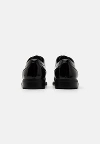 Scarpe in pelle verniciata nera con una finitura liscia e lucida, punta arrotondata e cuciture minime, dotate di una robusta suola nera.